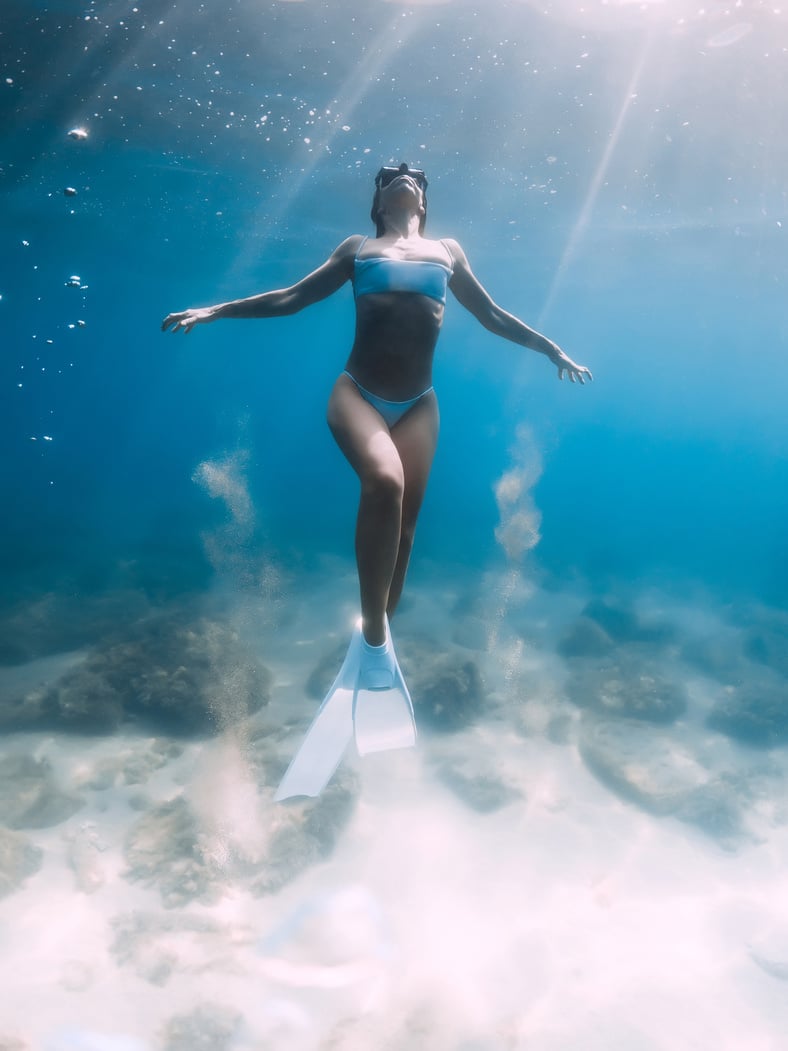 Freediver girl glides and posing over sandy sea with white freediving fins.